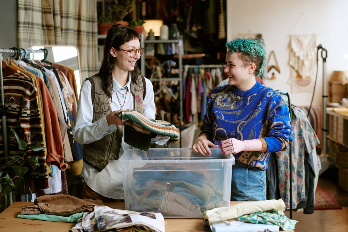 Two volunteers smiling while sorting secondhand clothes in a thrift store